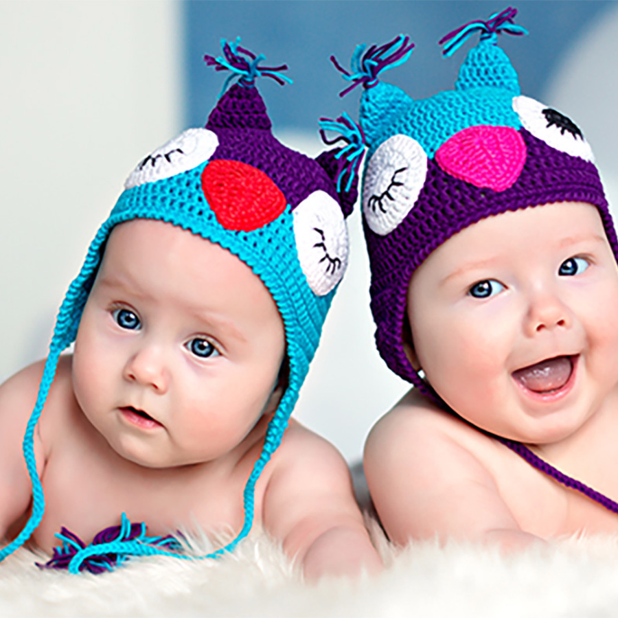 Newborn twins wearing owl hats.